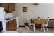 Compact kitchen with a stove, refrigerator, wooden cabinets, and a small dining table.