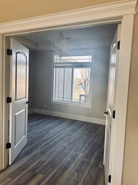 Bright empty interior room with gray flooring, two white doors, and a large window