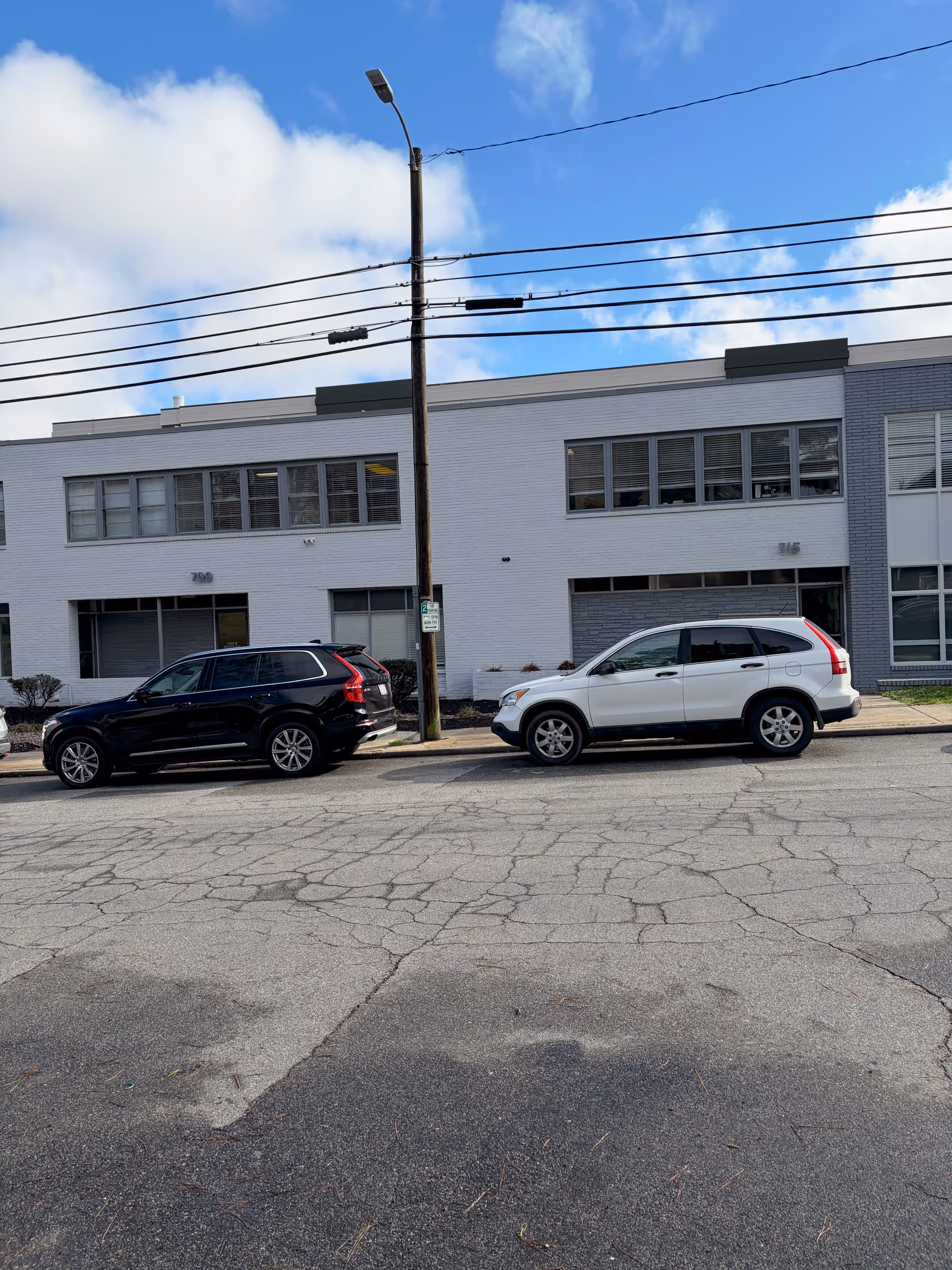 Exterior view of a white two-story building with parked cars on the street.