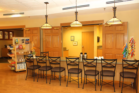 Long counter with eight high-back bar stools, pendant lights overhead, a snack display and wooden doors in a communal dining area.
