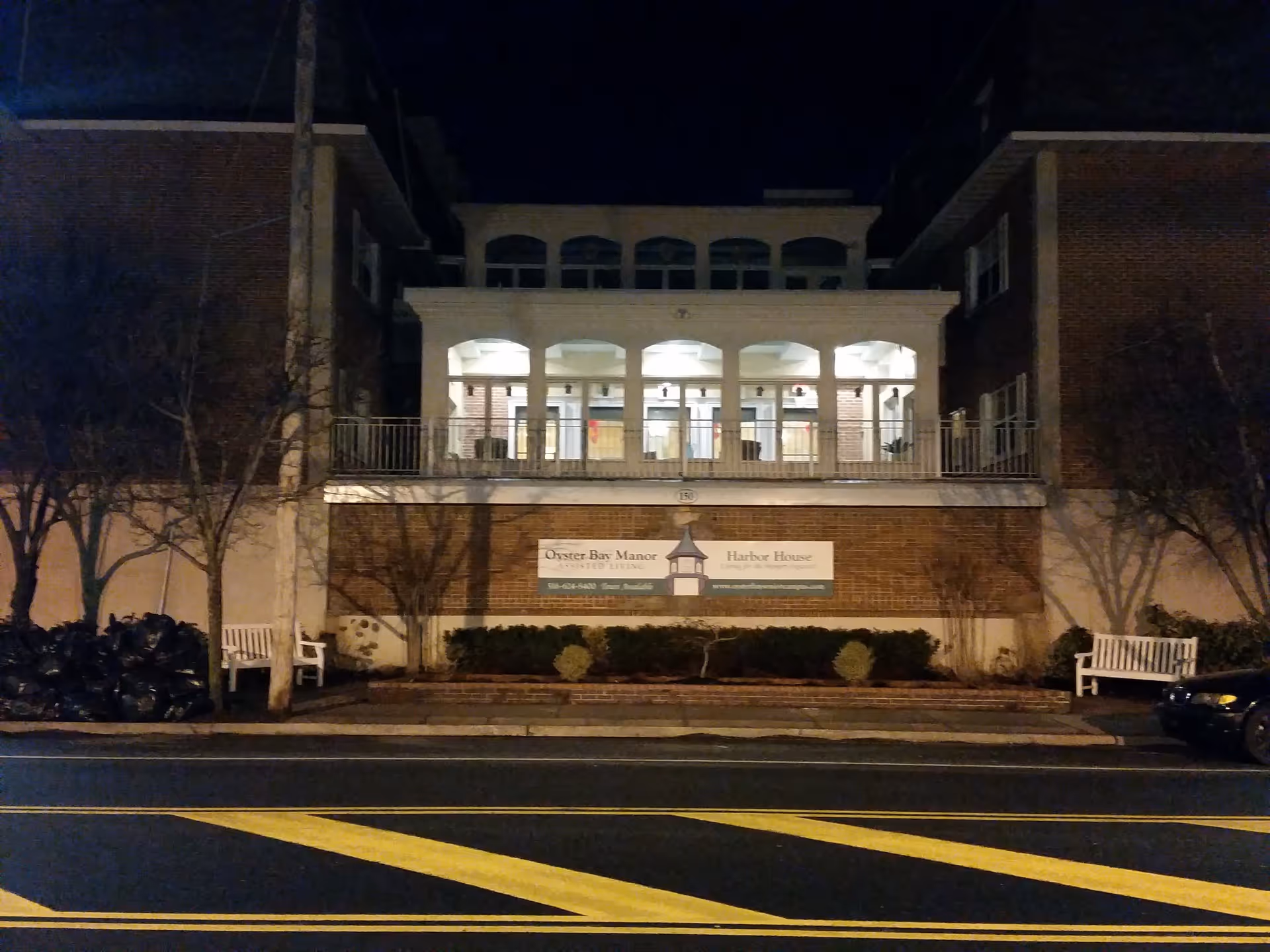 Nighttime exterior view of Harbor House Assisted Living with a brick building and arched balcony.