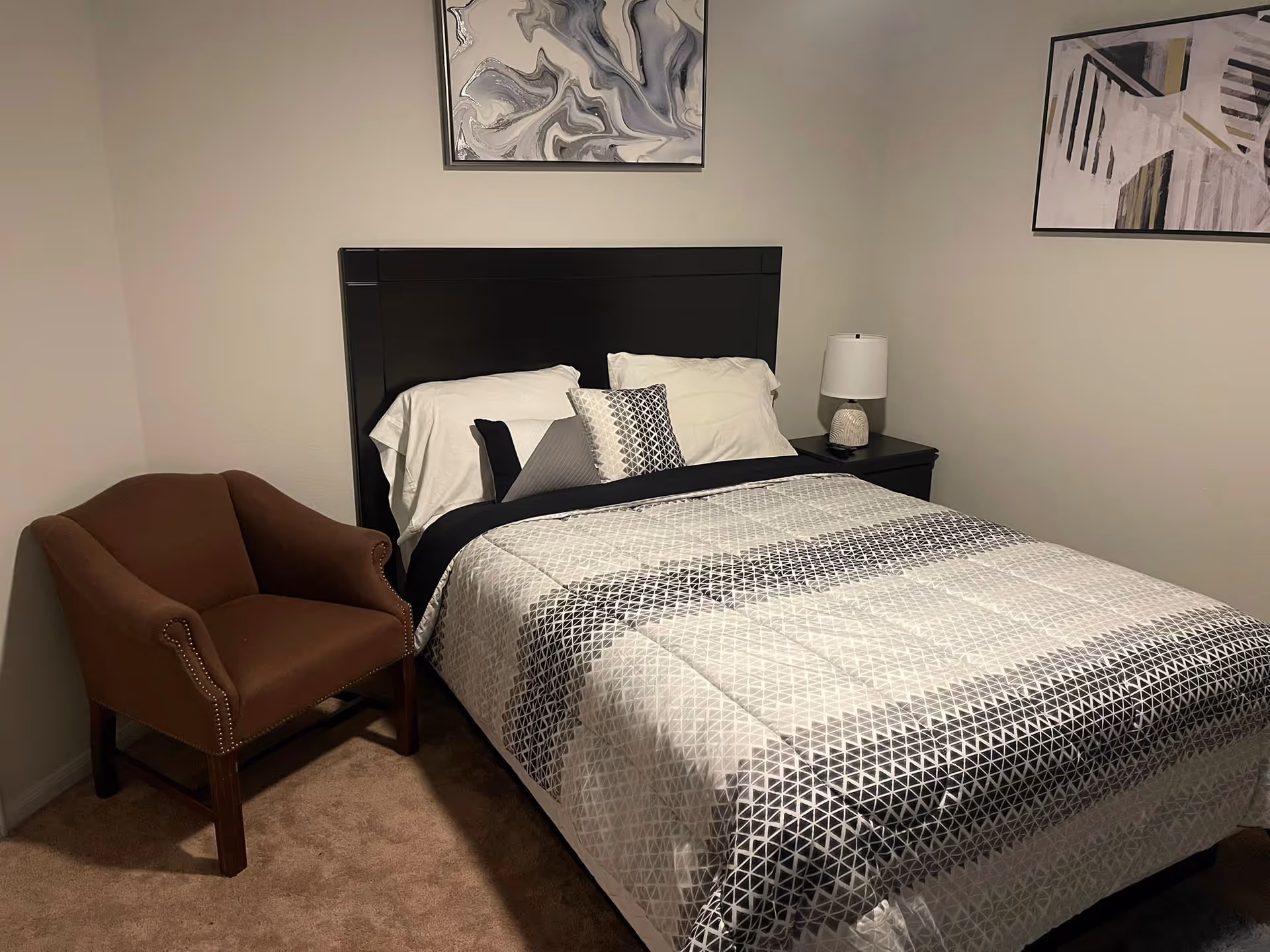 A neatly made bedroom in a senior living facility with bed, nightstand, lamp, and chair.