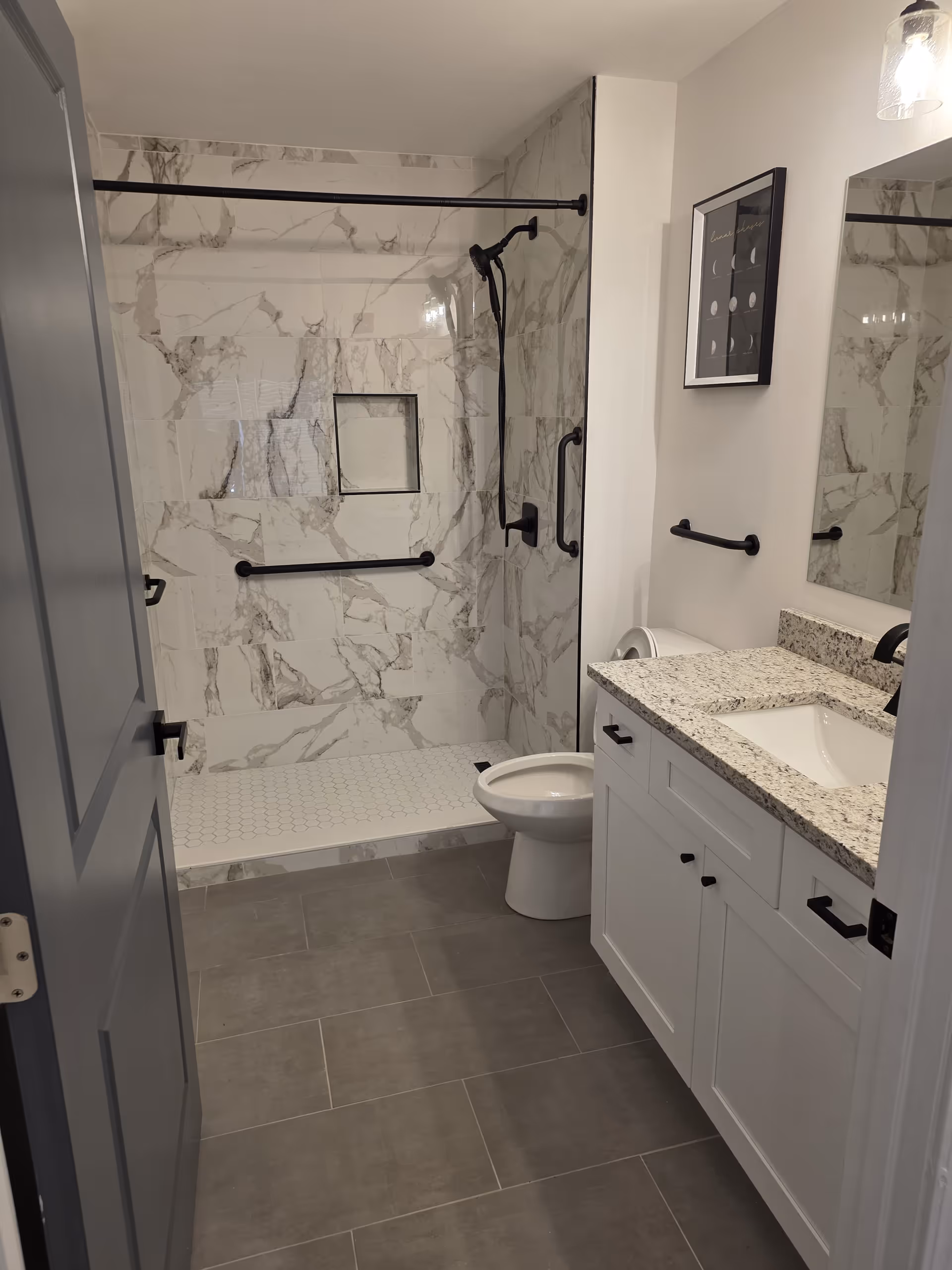 Walk-in shower with marble walls, grab bars, and granite vanity in a senior living facility.