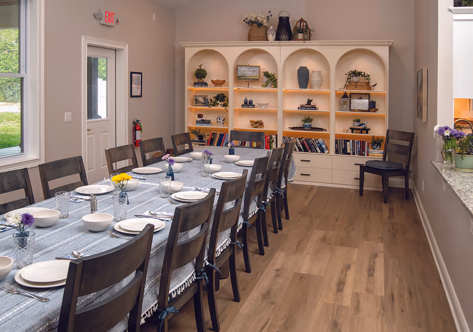 A long dining room table set for a meal with a built-in bookcase along the wall.