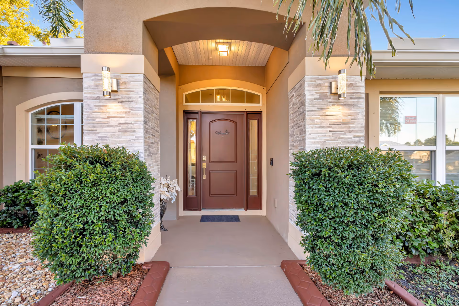 Residential facility entrance with brown door, stone siding, and manicured shrubs.