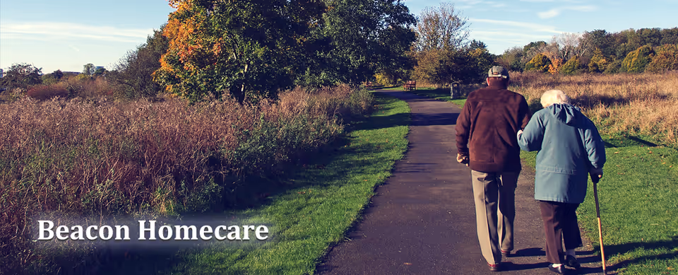 An elderly couple walks along a park path outdoors, with Beacon Homecare watermark.