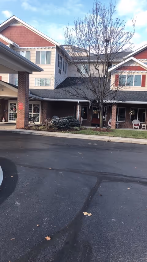 Front exterior of AAACare Columbus senior living facility with a tree and entrance seating.