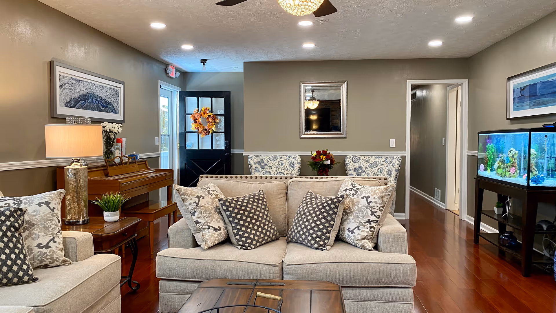 Cozy living room with beige sofa, patterned cushions, a piano, and a bright fish tank.