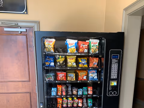Snack vending machine with assorted chips and beverages inside a hallway.
