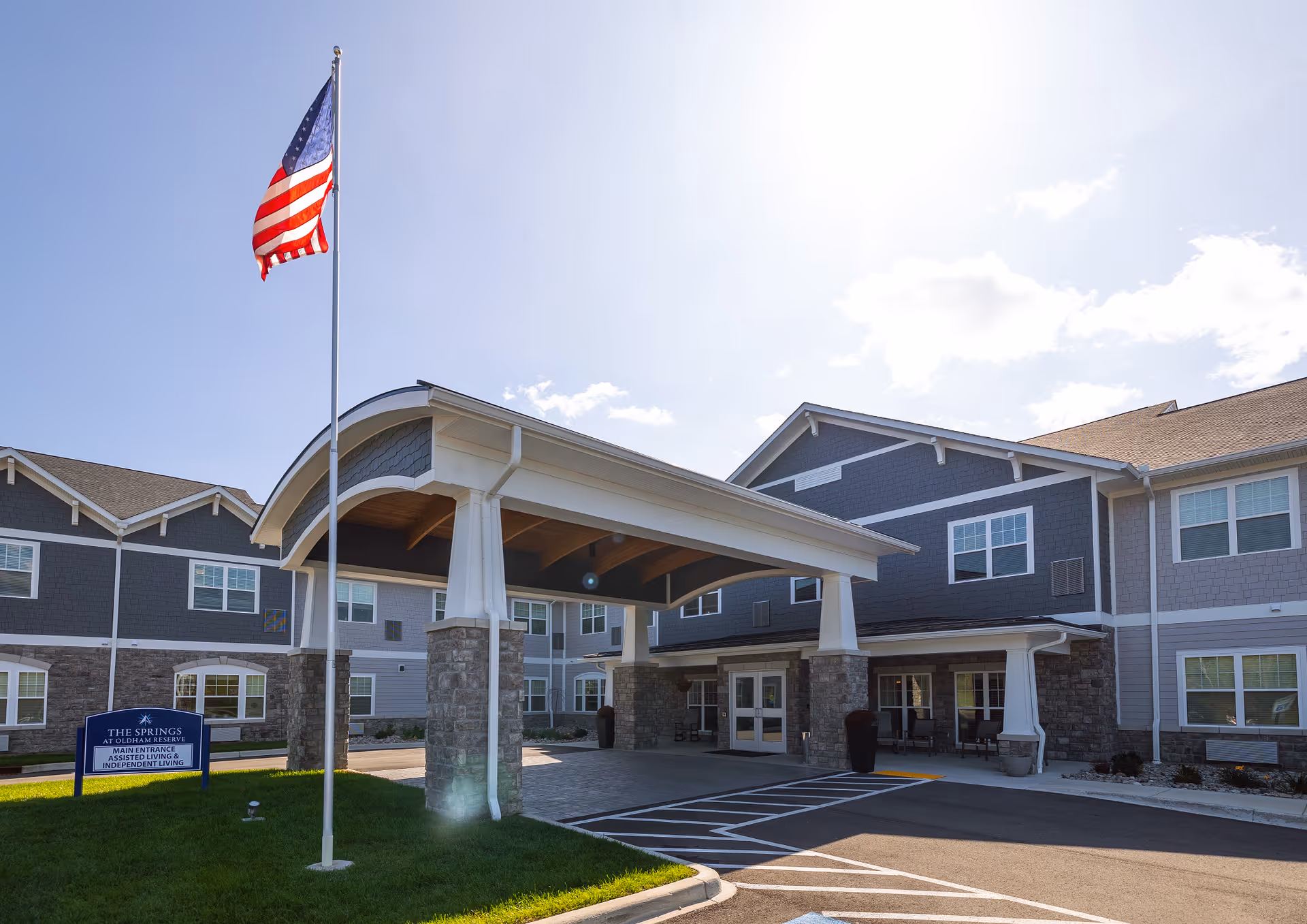 Front entrance of a senior living facility with a covered porte-cochère, American flag, and multi-story building exterior.