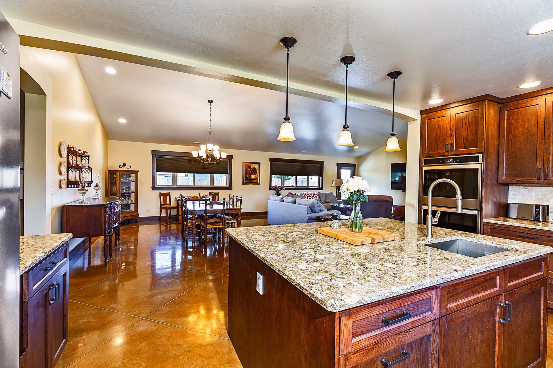 Open-concept kitchen with granite island, rich wood cabinets, and adjoining dining and living spaces.
