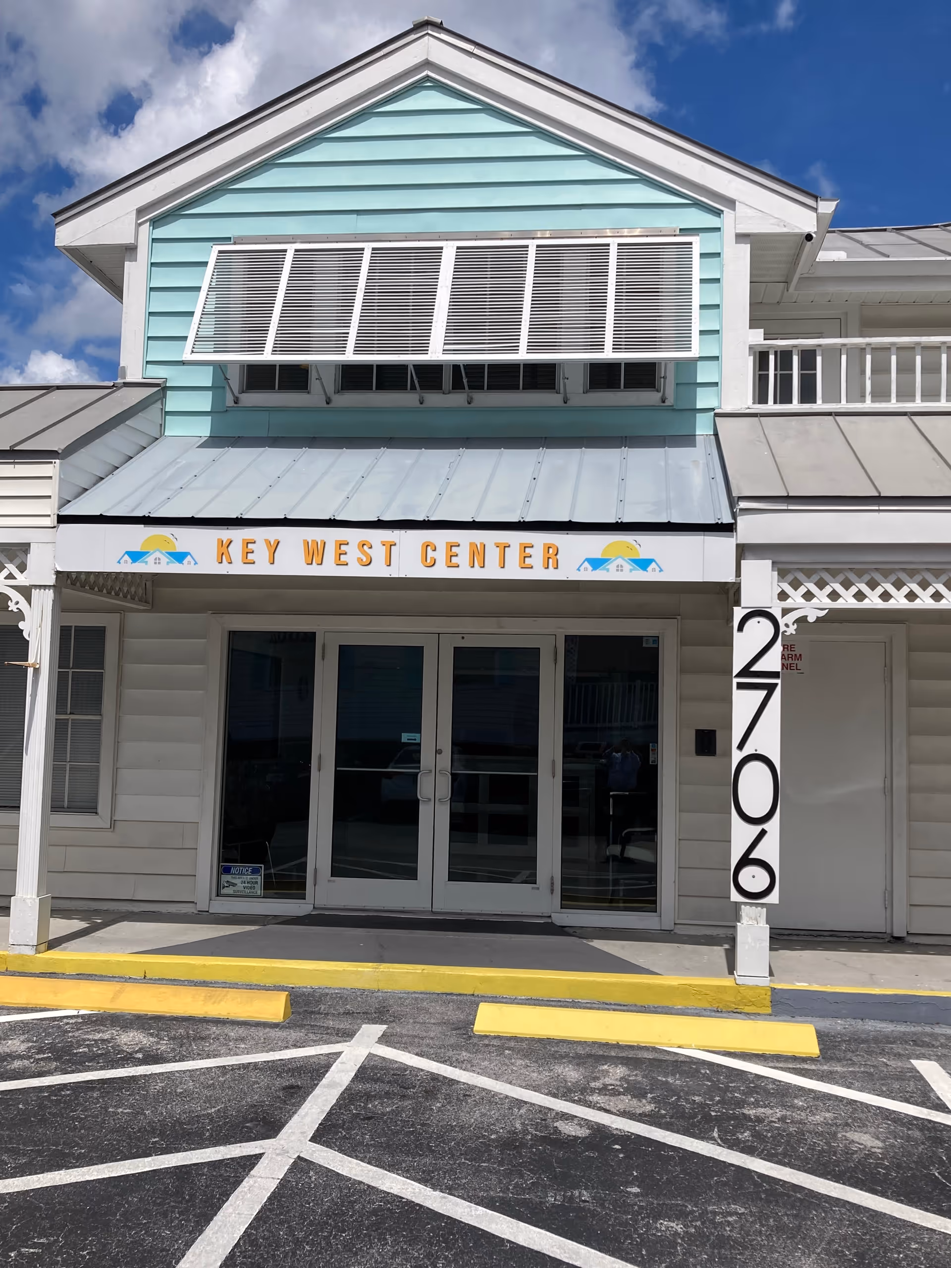 Exterior view of a pastel teal building with Key West Center sign and glass doors.
