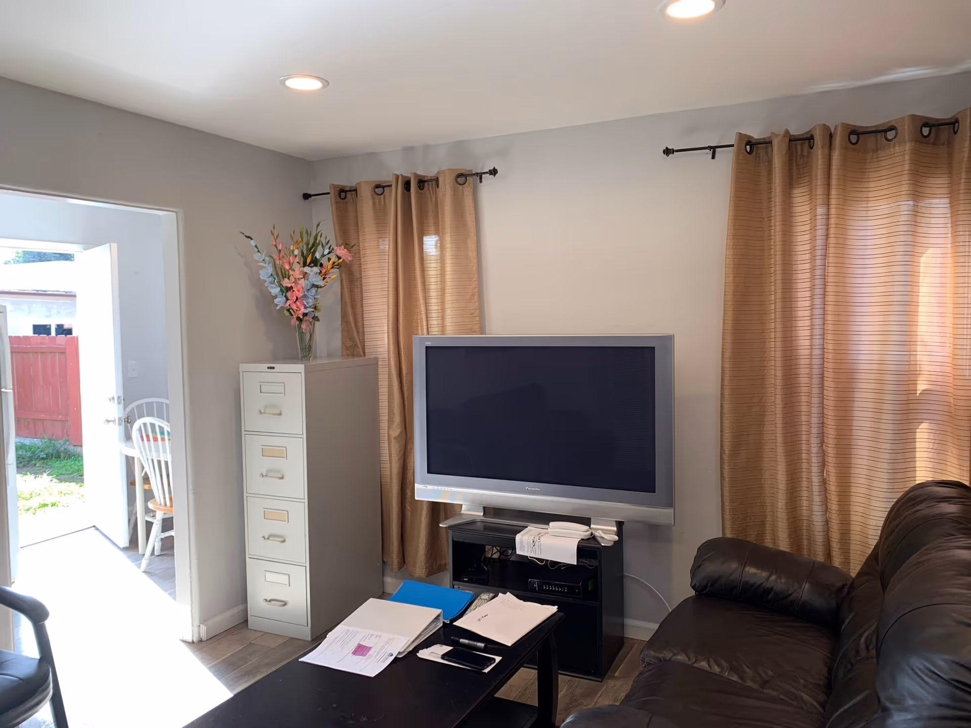 Living room featuring a large TV on a stand, beige curtains, and a brown leather sofa.