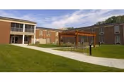 Exterior brick senior living building with lawn, walkway, and a wooden pergola seating area.