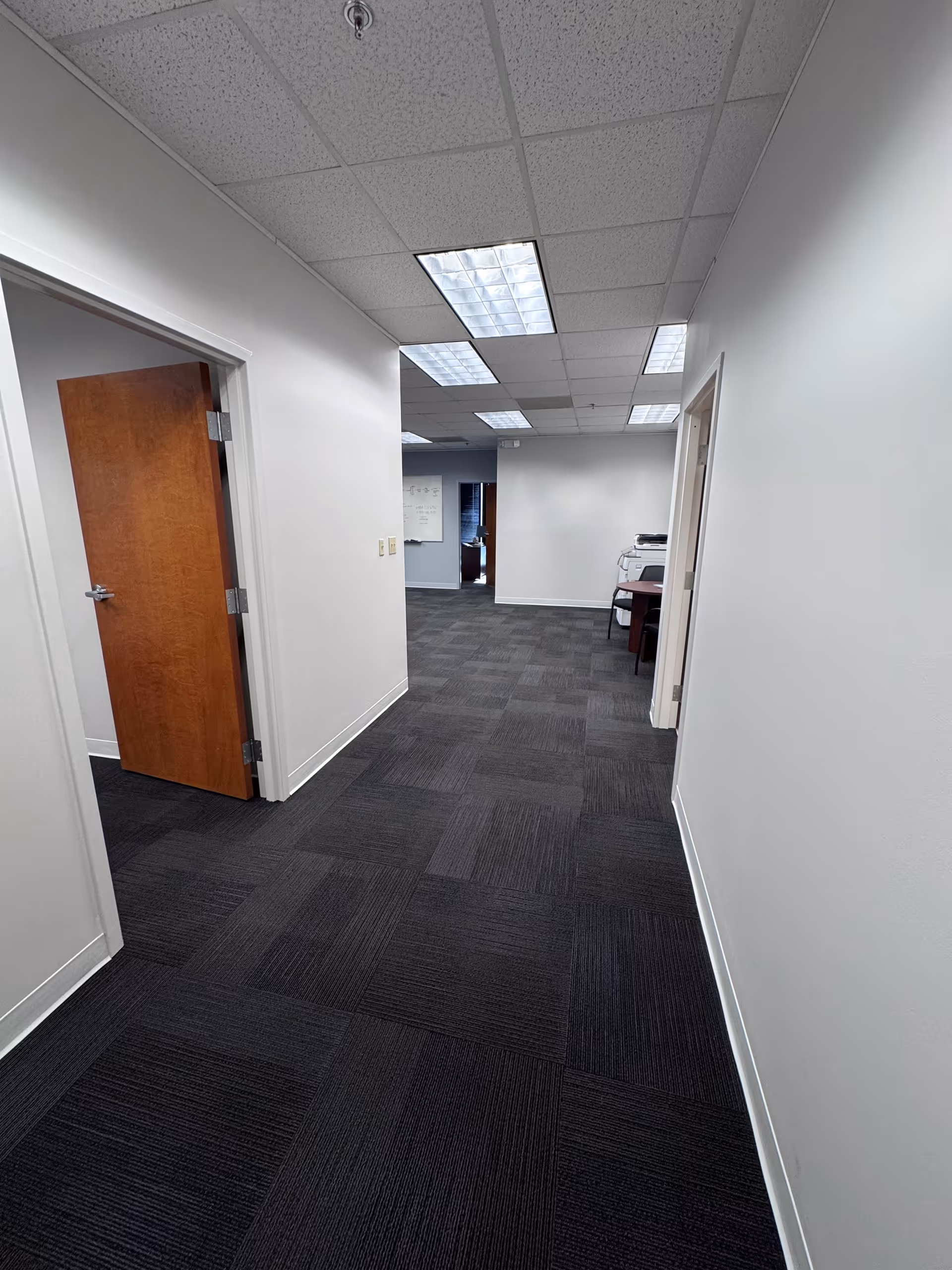 White-walled facility hallway with dark carpet, doors, and overhead fluorescent ceiling lights.