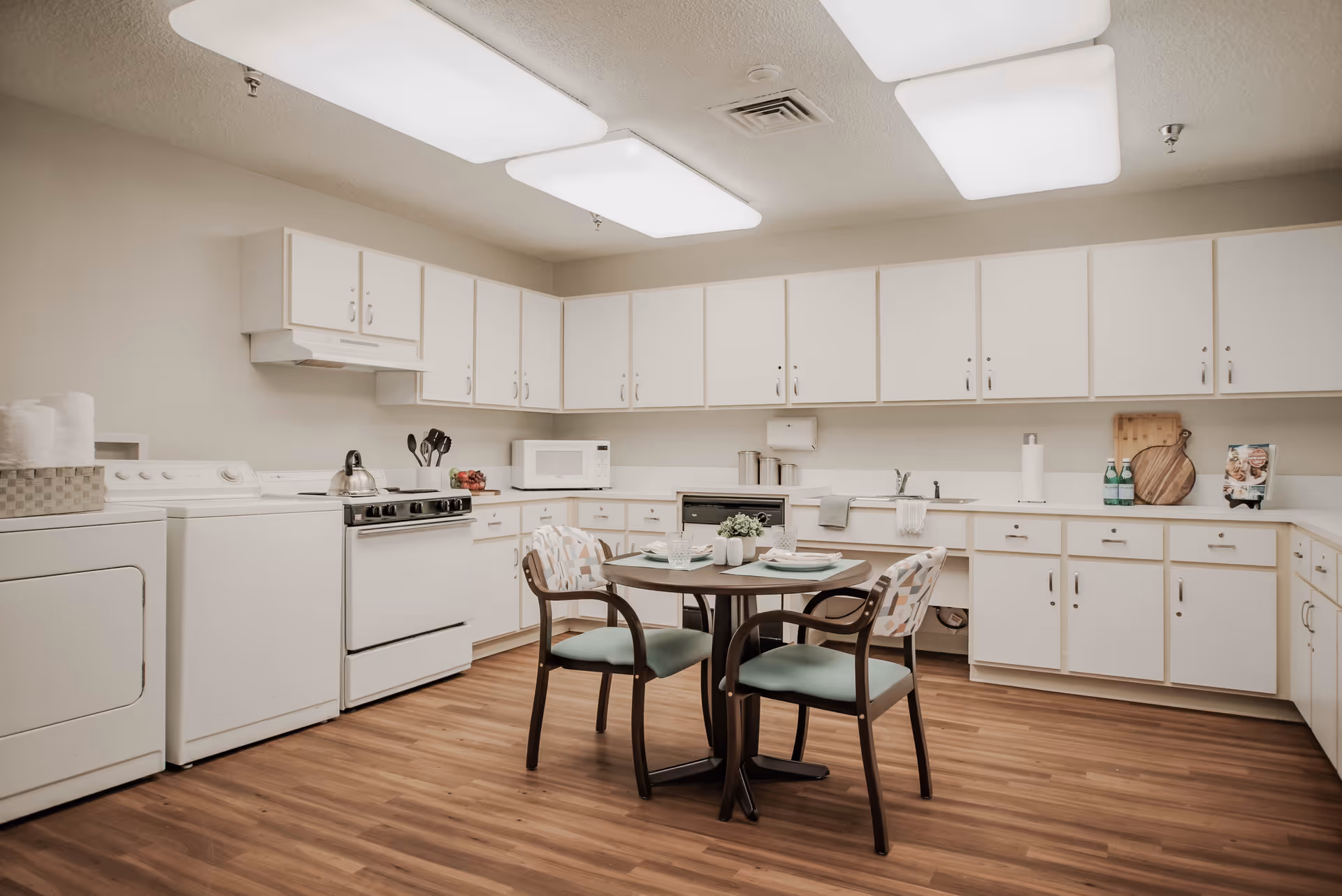 Bright white kitchen with cabinets, appliances, and a small round dining table with chairs.