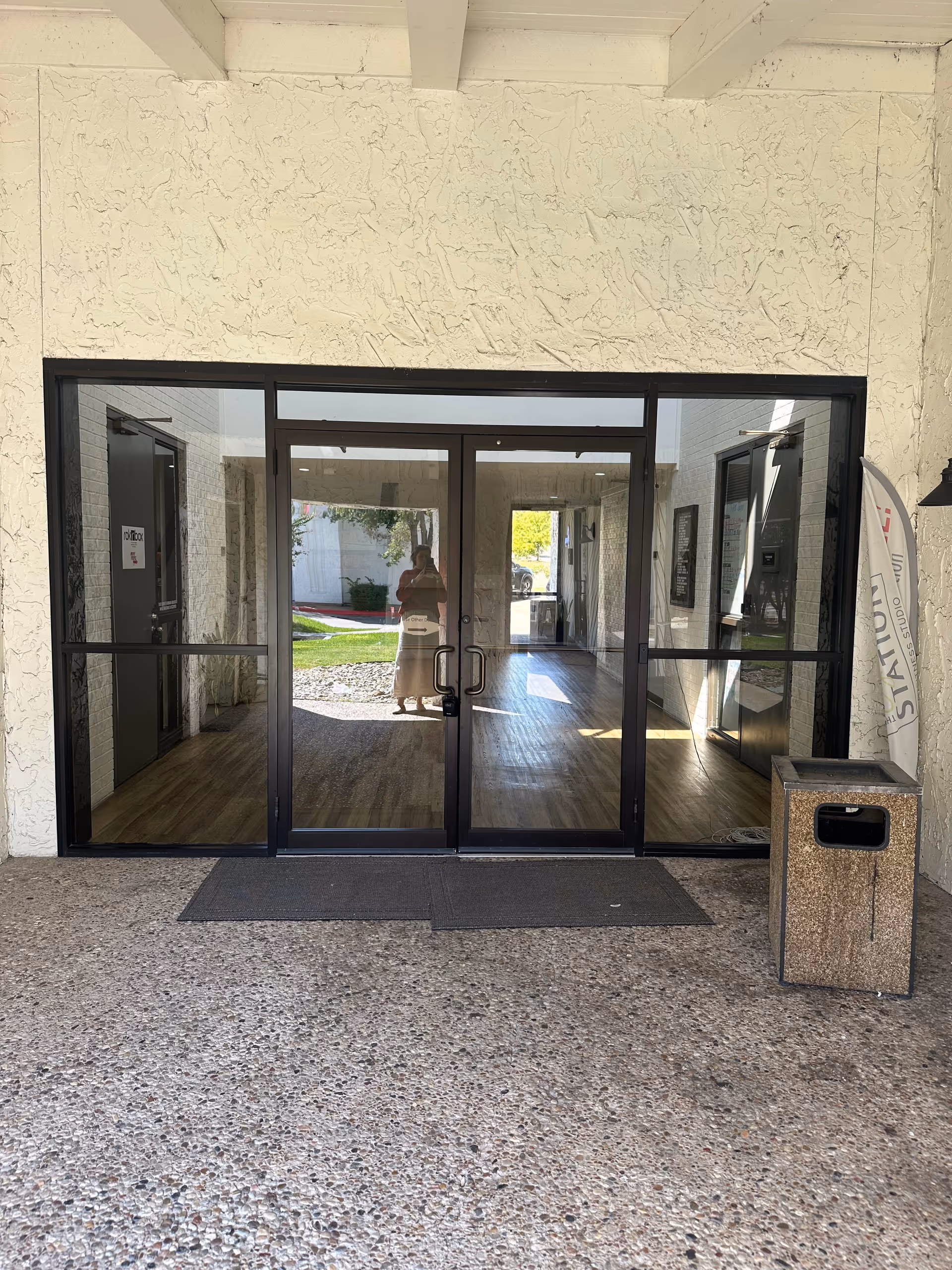 Glass front doors open to a lobby, framed by white textured exterior walls.