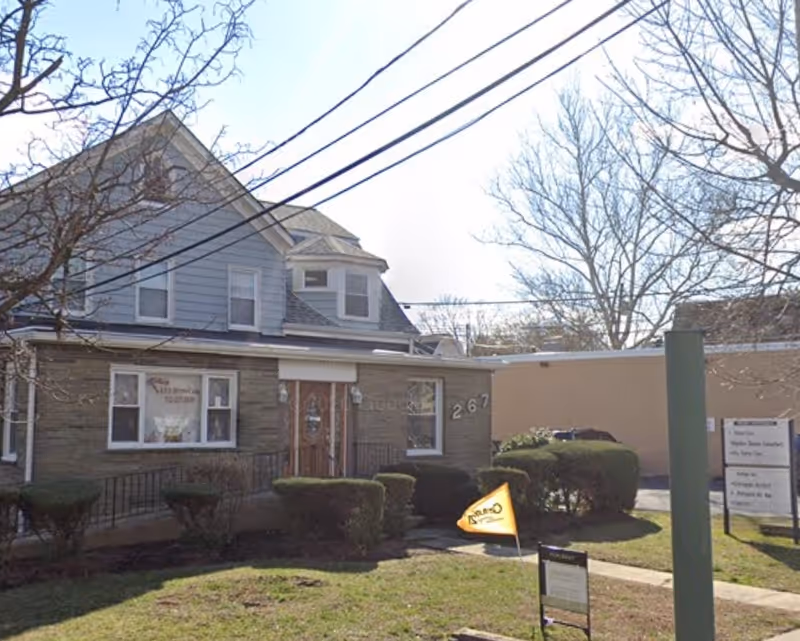 Two-story building front with entrance, signage, and trimmed shrubs outside, resembling a senior home.