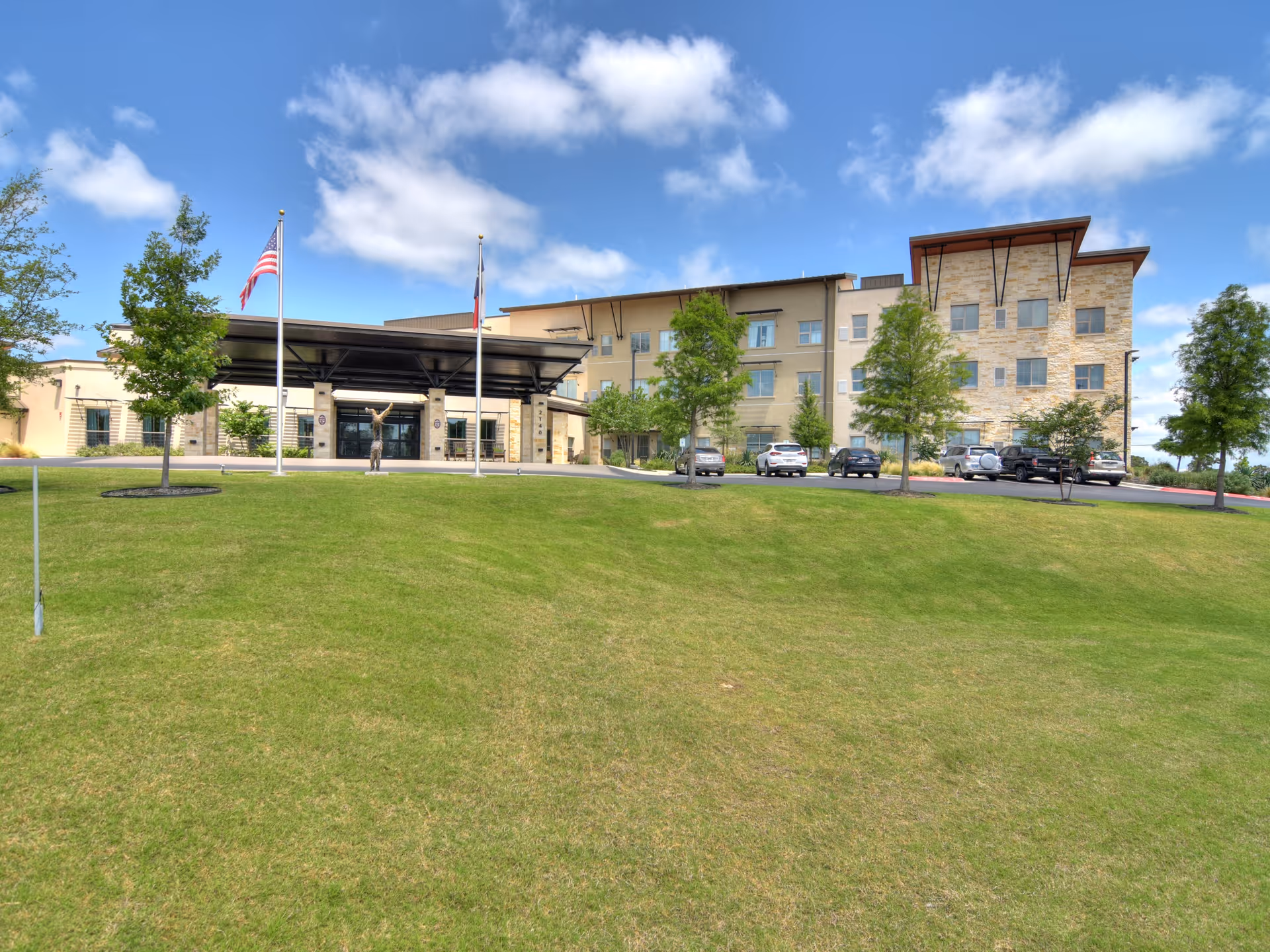 Exterior view of Élan Westpointe at New Braunfels with lawn, entrance, and parked cars.