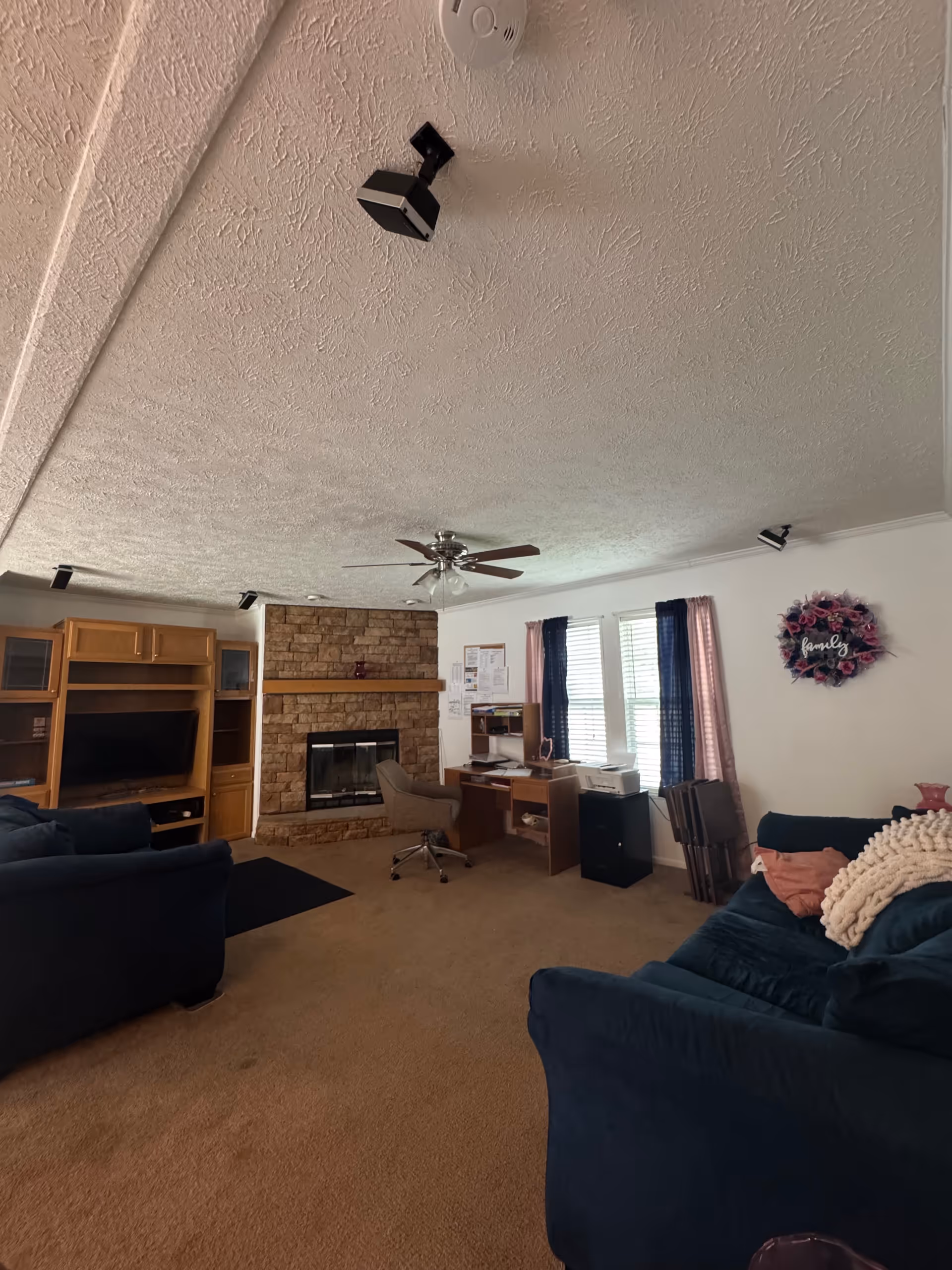 Living room in Sonny Senior Care Assisted Living with fireplace, TV cabinet, desks, and blue couches.