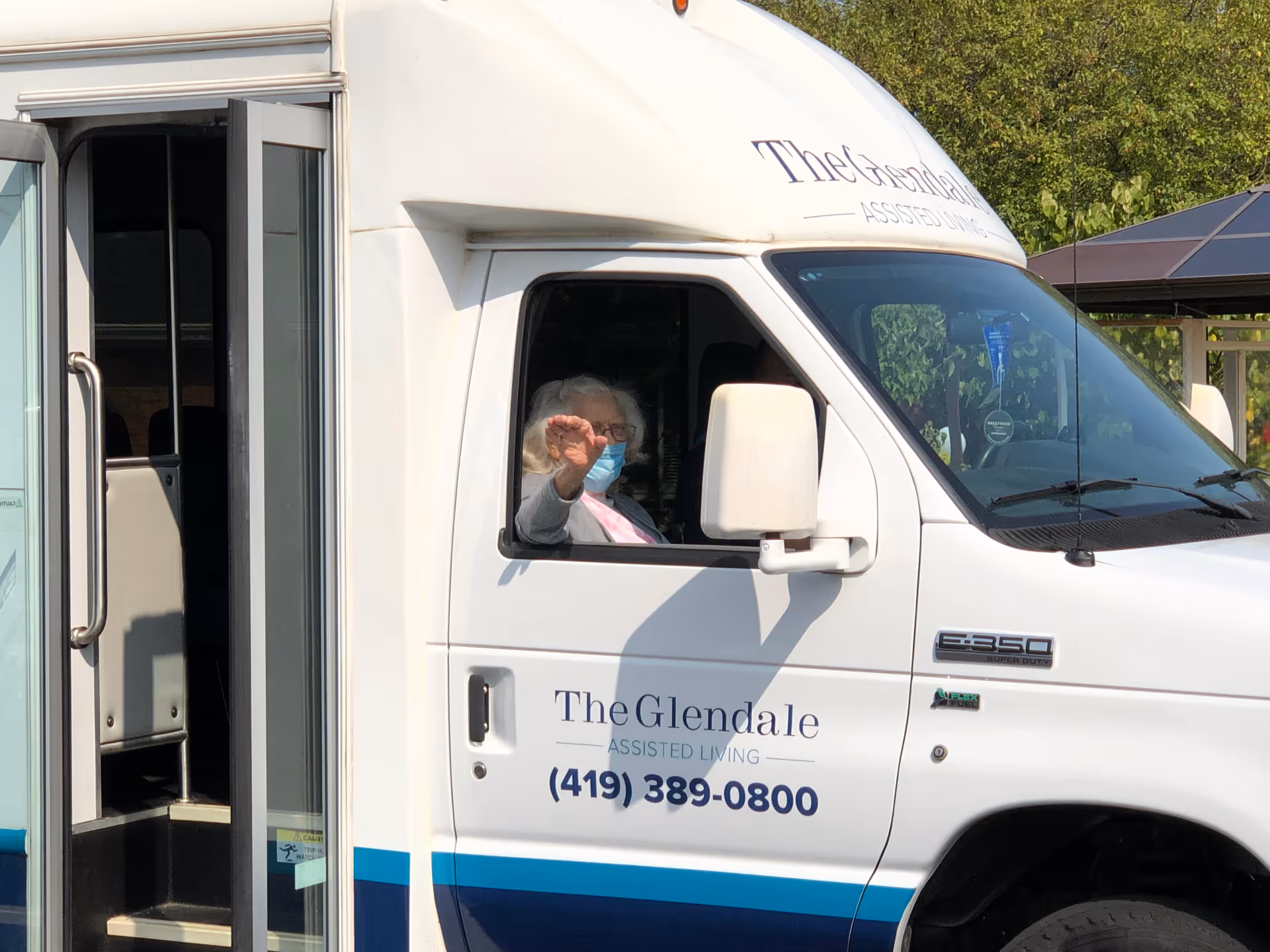 White assisted-living transport van with a masked passenger visible in the driver's seat