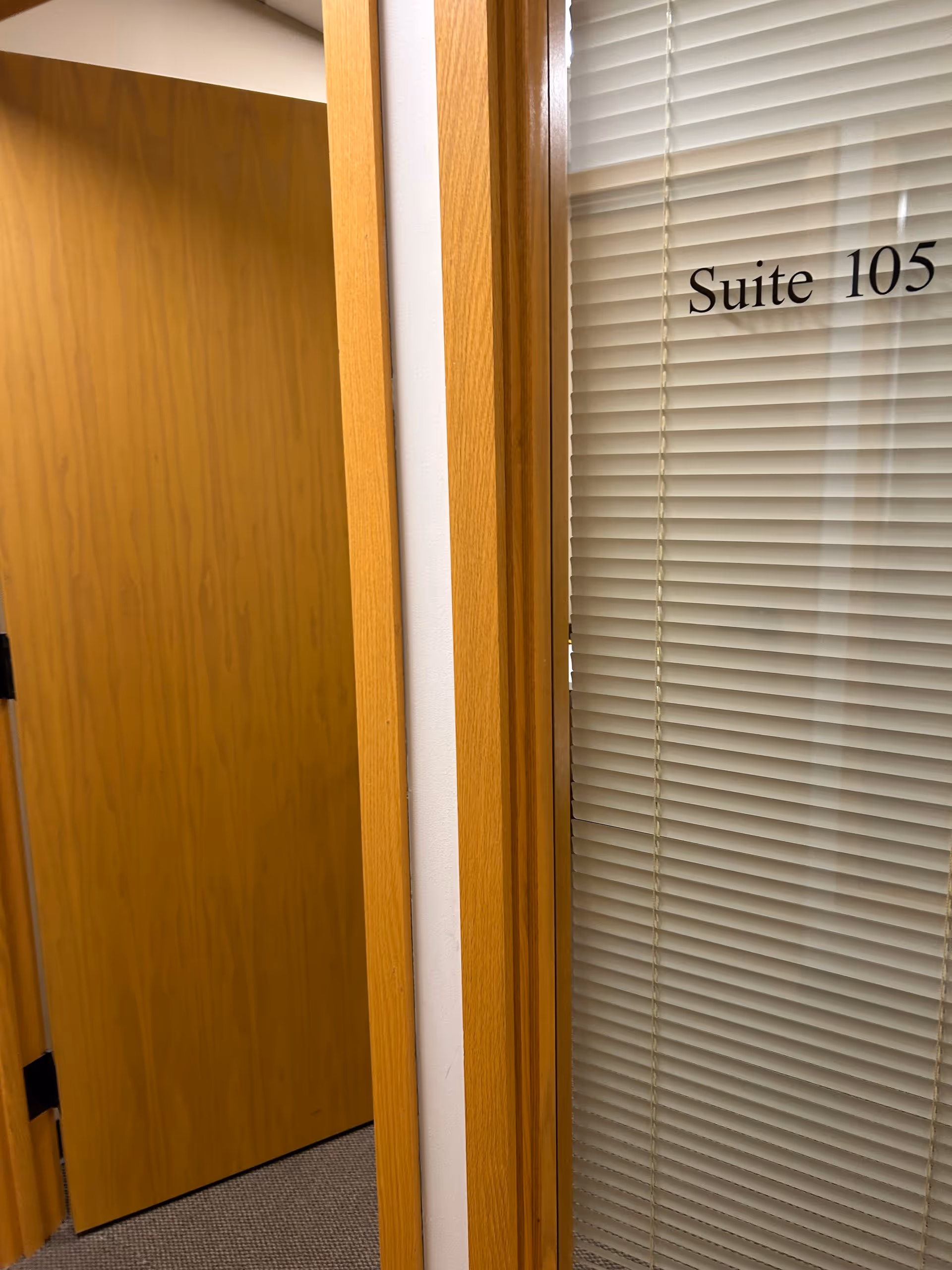 Wood-framed doorway with blinds on glass door reading Suite 105.