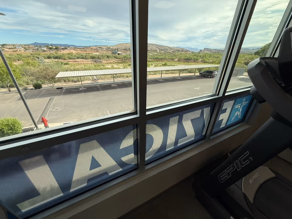 Indoor gym space with treadmill near large windows overlooking desert landscape.
