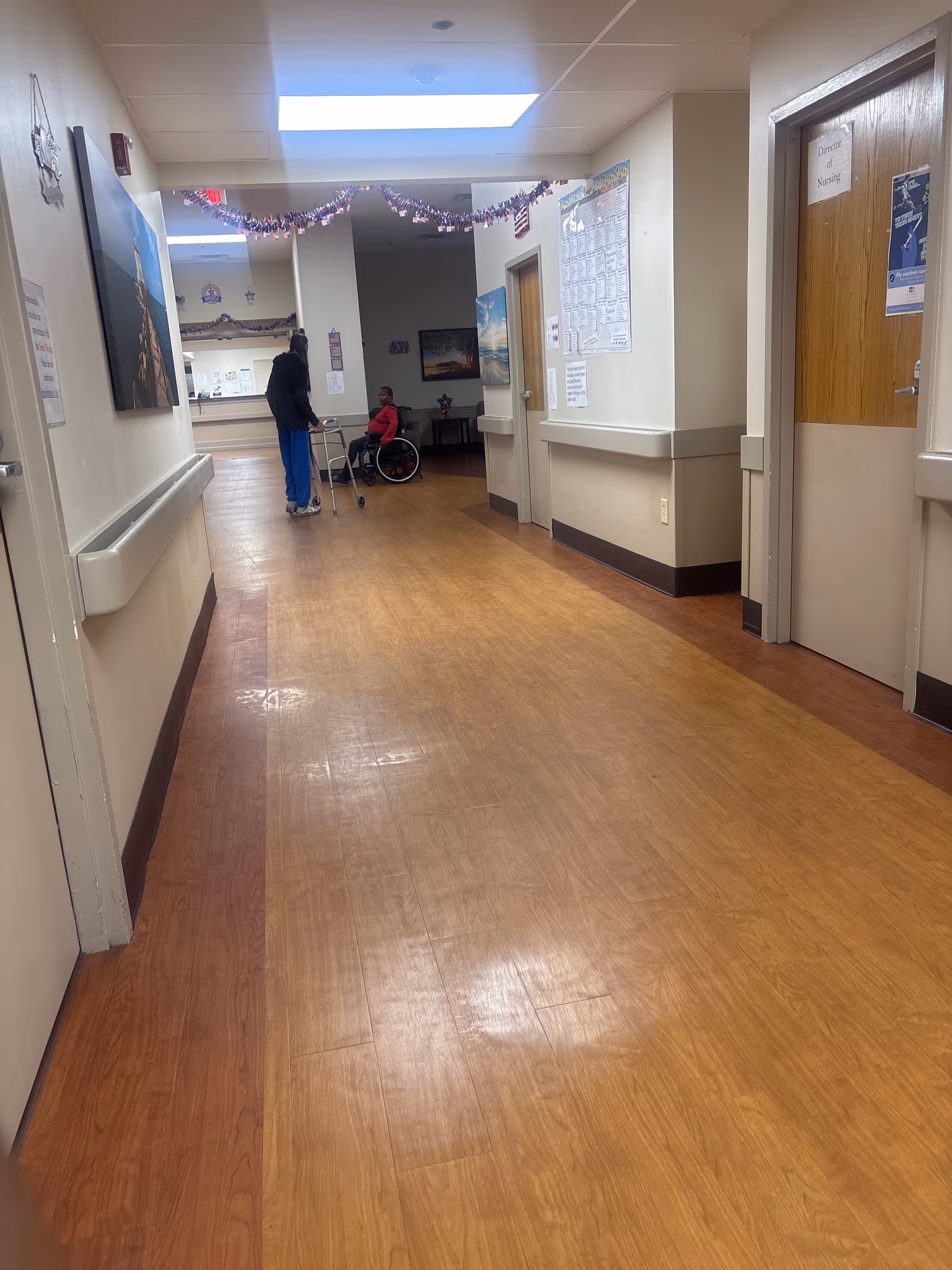Long hallway in a senior care facility with a person in a wheelchair and another standing.
