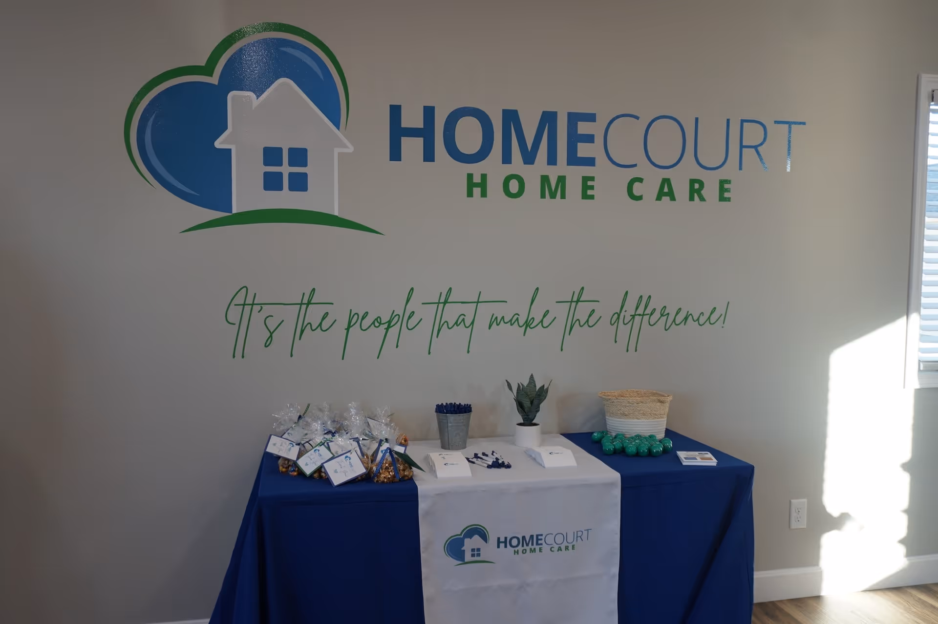Interior lobby area with HomeCourt Home Care logo and a blue-draped display table.