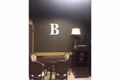 Dark dining area with a round table, four chairs, lamp, and a wall letter B