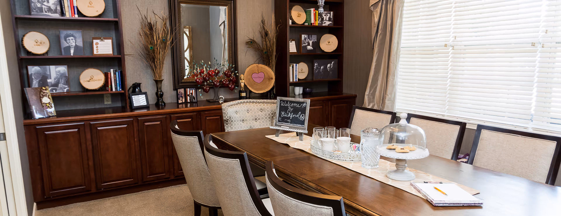 A long dining table with chairs and a display cabinet in a bright dining room.
