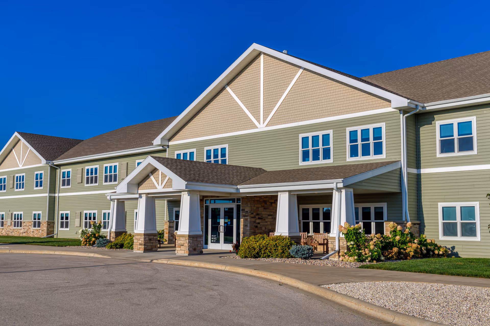 Green, multi-wing senior living facility exterior with entrance and landscaped surroundings
