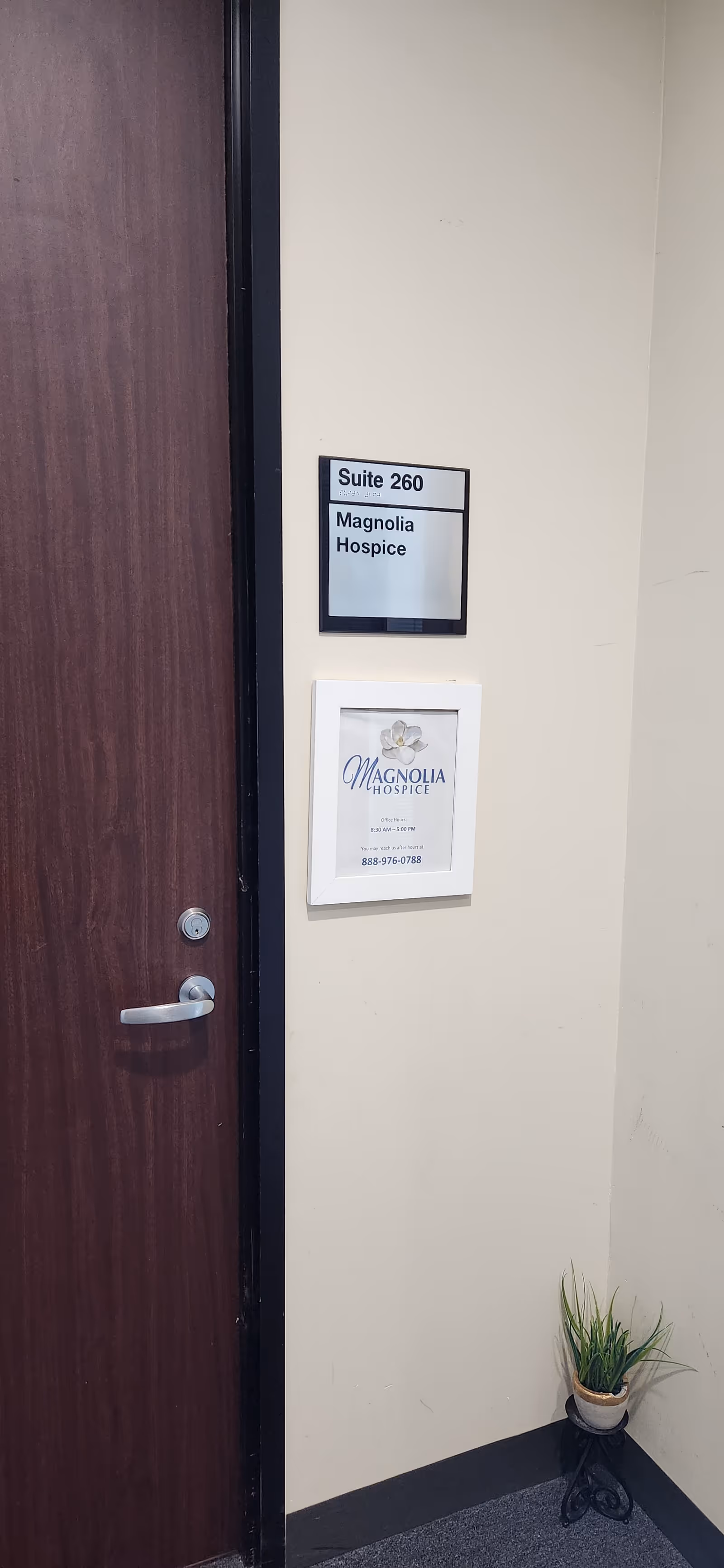 Interior hallway door with Magnolia Hospice suite sign and small potted plant beside wall.