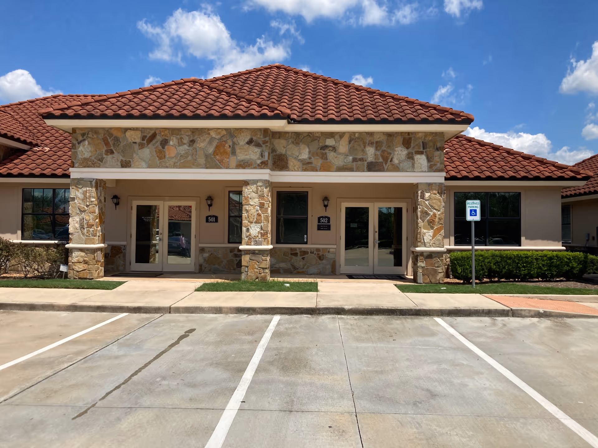 Stone-faced senior living facility entrance with red-tiled roof and a front parking lot