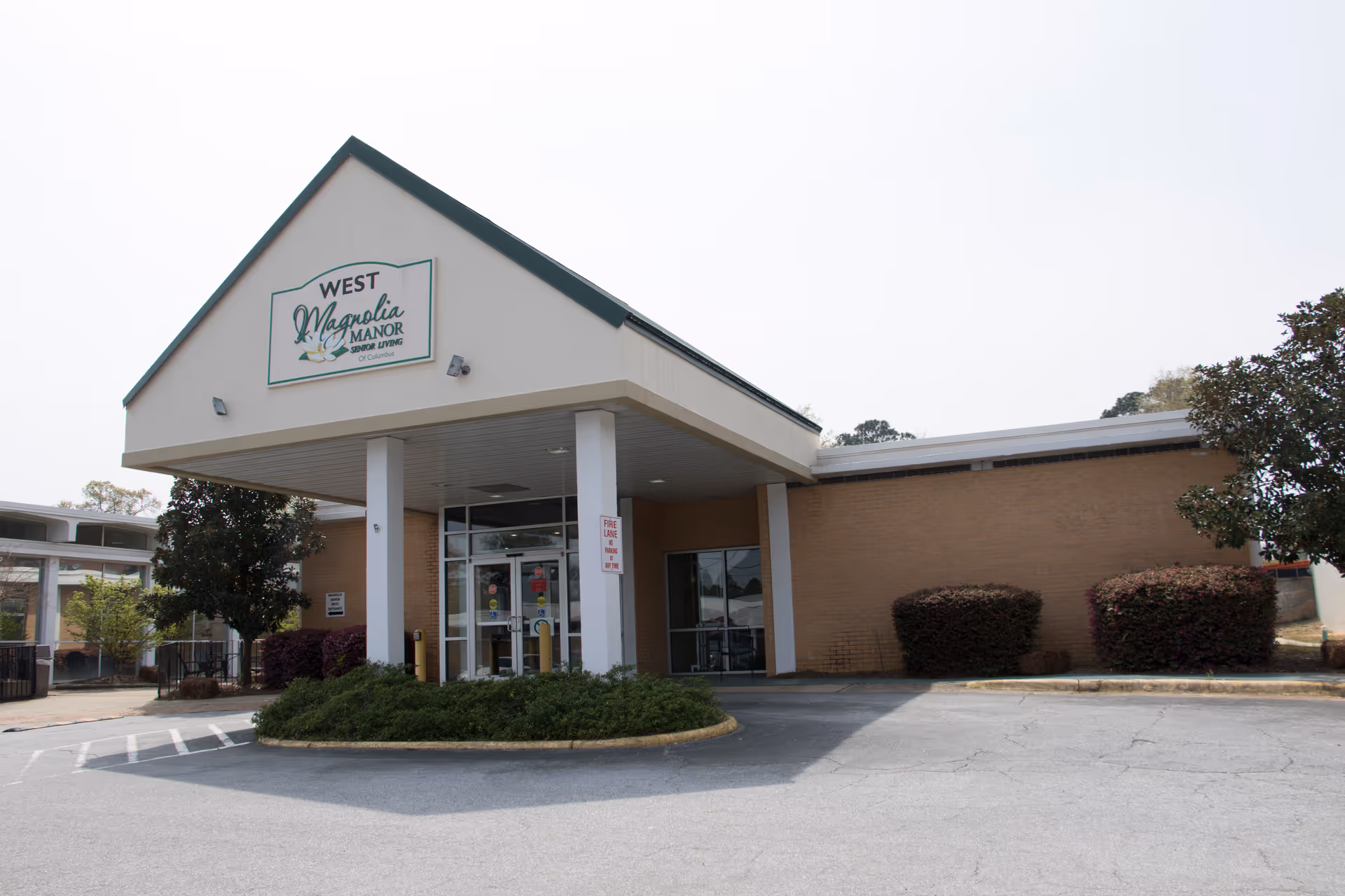 Front view of Magnolia Manor of Columbus Nursing Center entrance with sign and shrubs.