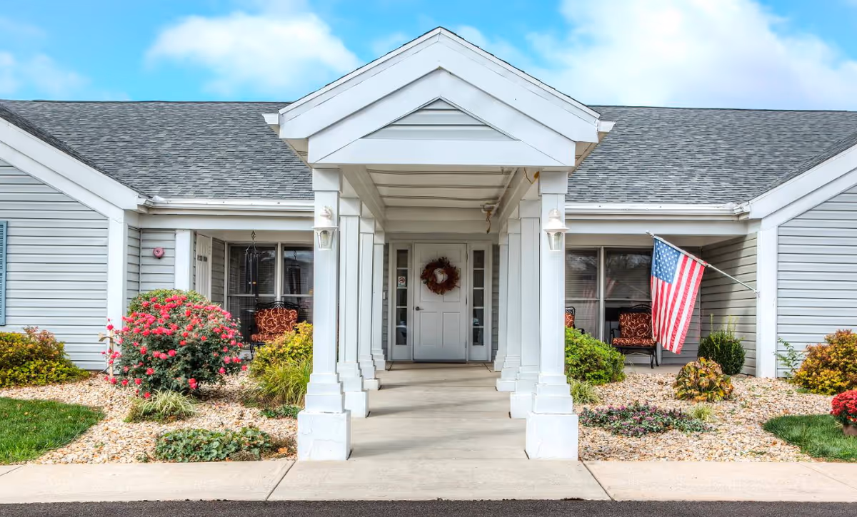Senior living facility front entrance with columns, landscaped garden, and an American flag.