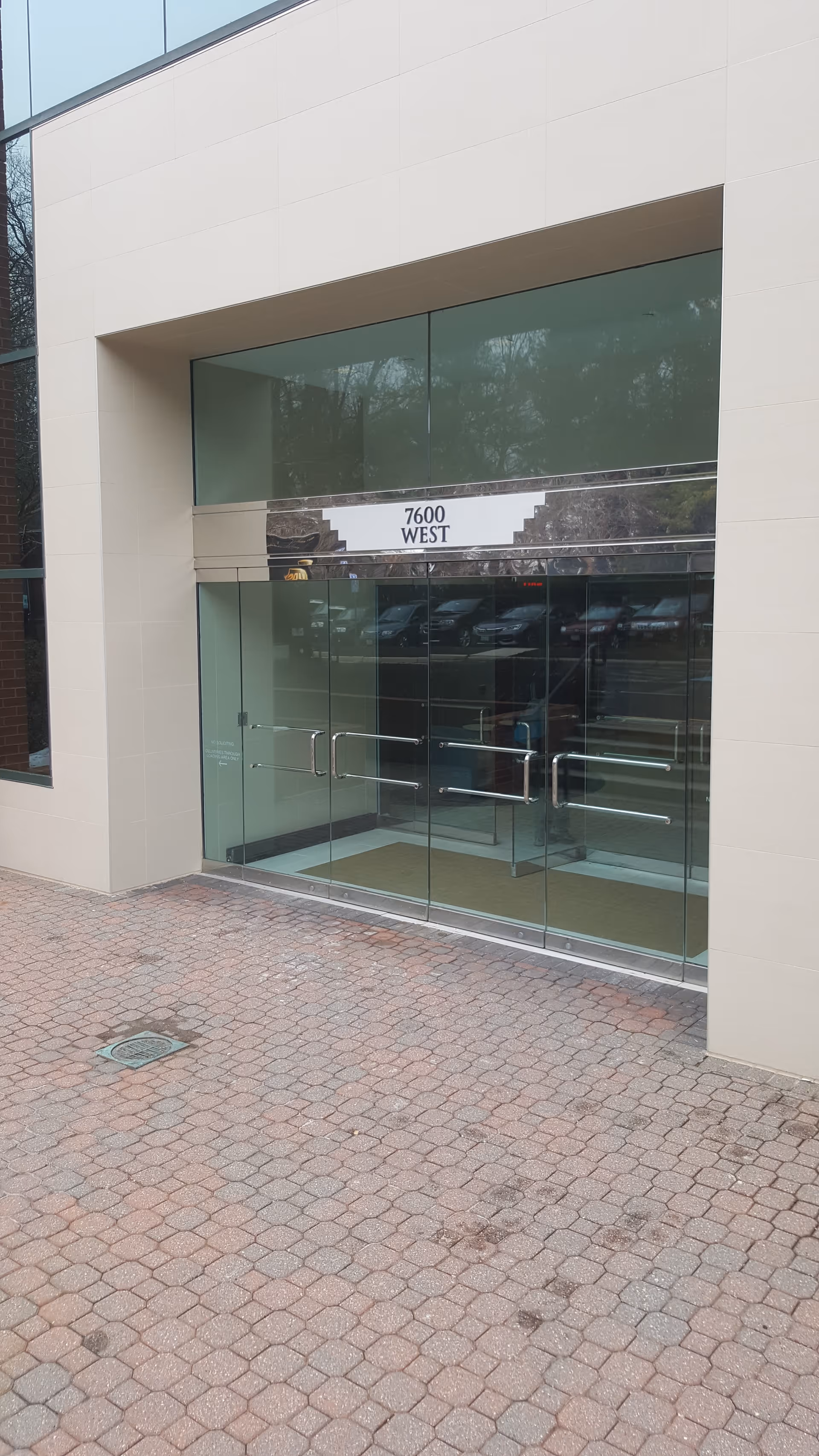 Glass double doors at a modern beige building entrance with a brick walkway