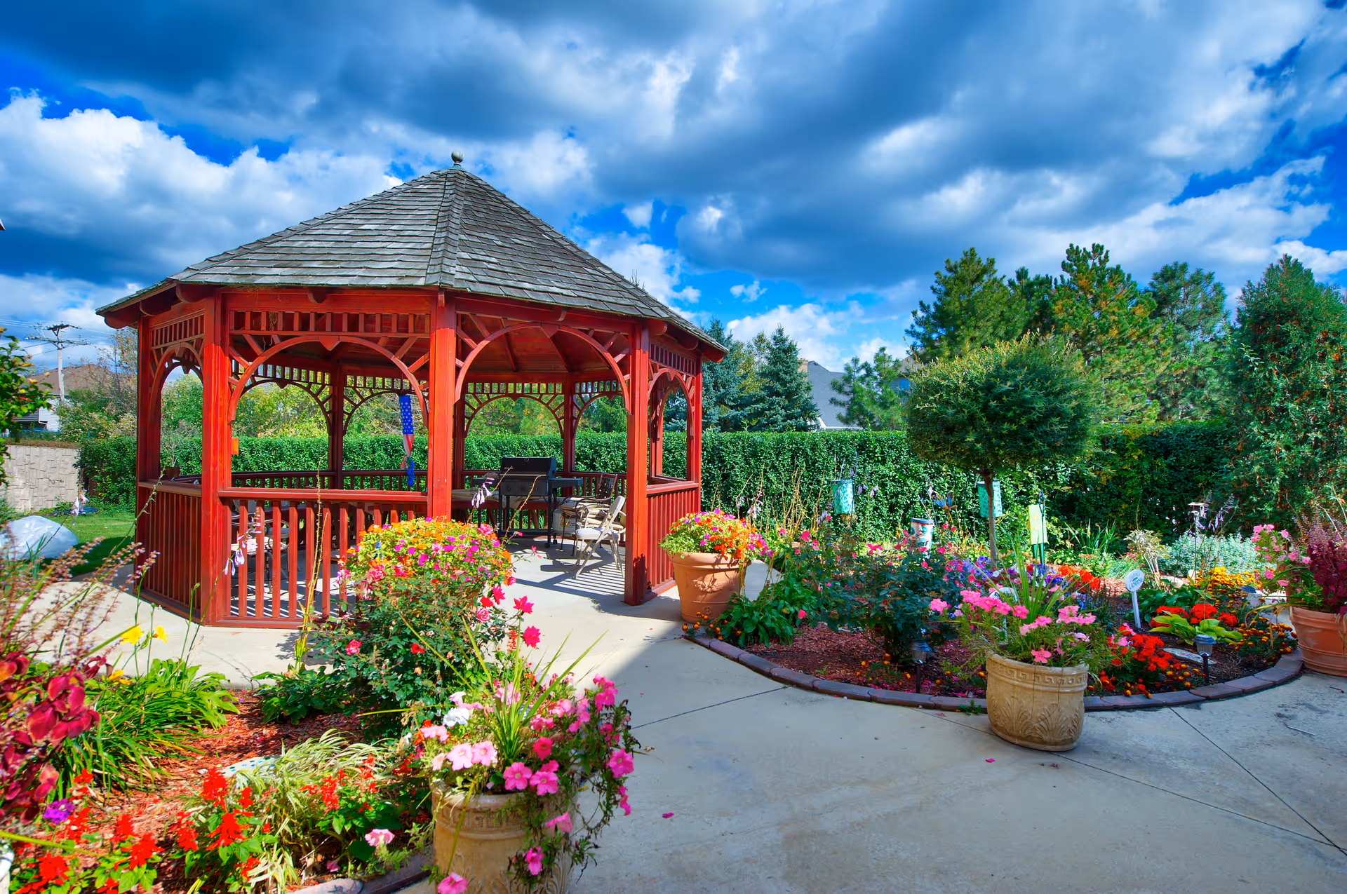 Red wooden gazebo amid vibrant flower beds in a sunny outdoor garden.