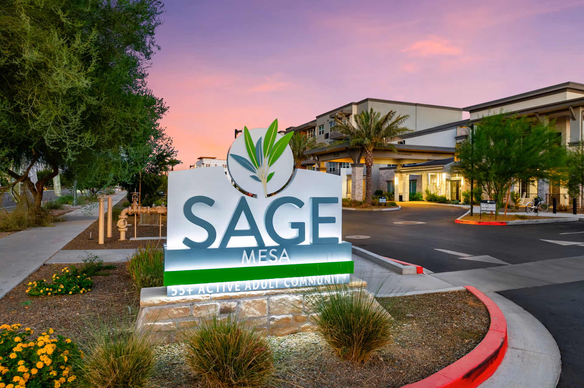 Sage Mesa senior living entrance with a large sign, landscaped foreground, and sunset sky.