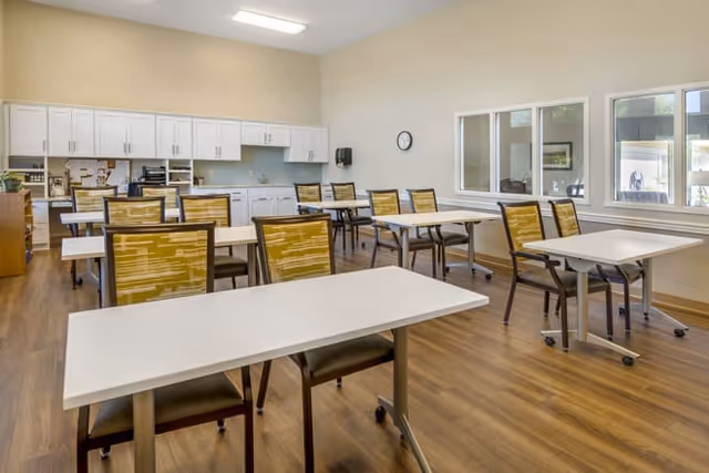 Bright dining area with several tables and chairs in a senior living facility.