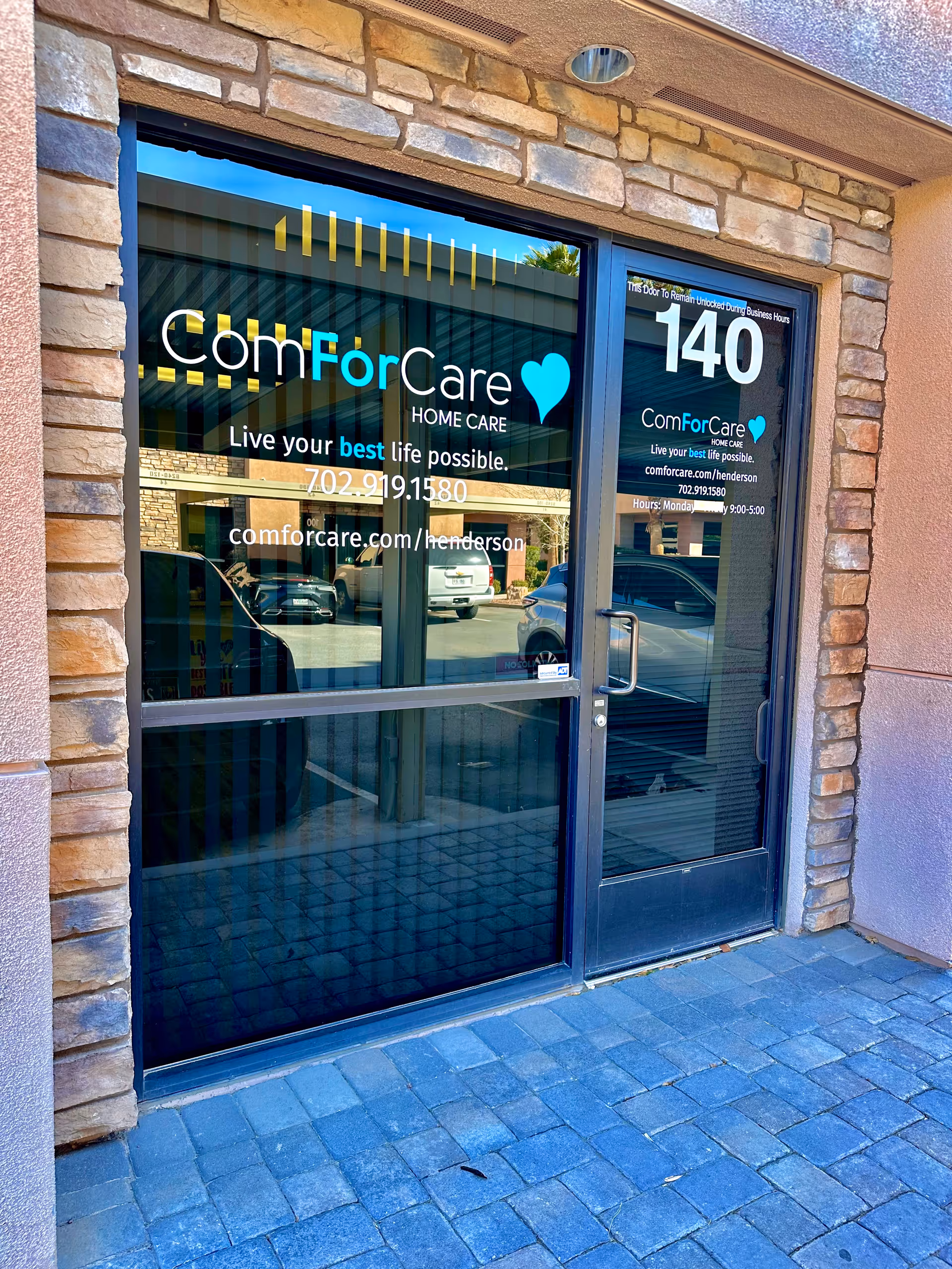 Glass entry door with ComForCare Henderson signage, stone facade, and reflected parking lot.
