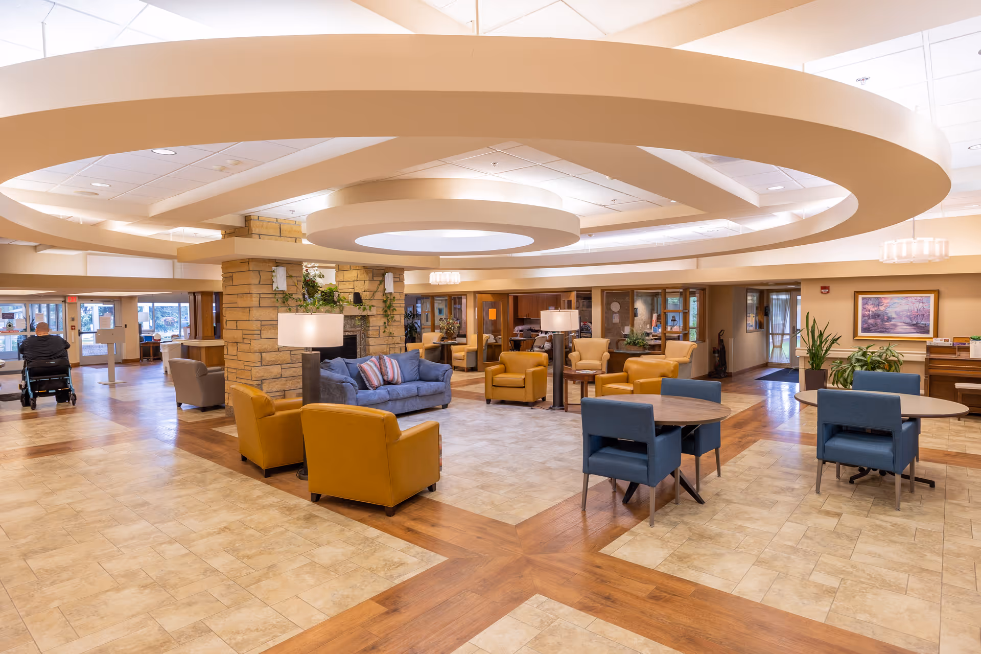 Spacious, well-lit senior living facility lobby with multiple seating areas, round ceiling fixtures, and tables.