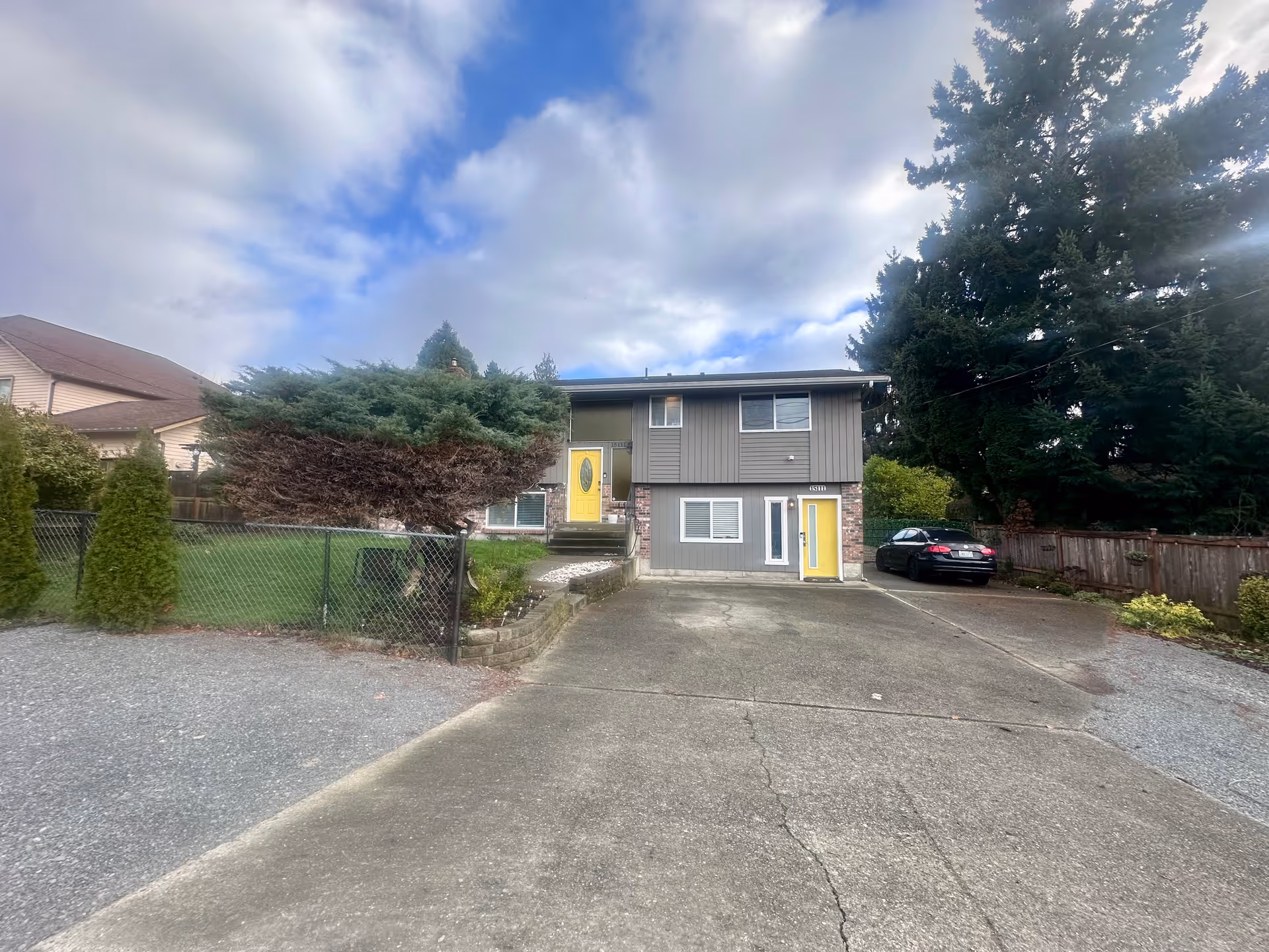 Exterior view of a grey senior living building with two yellow doors and driveway.