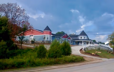 Exterior view of The Rose House senior living facility along a curved driveway.