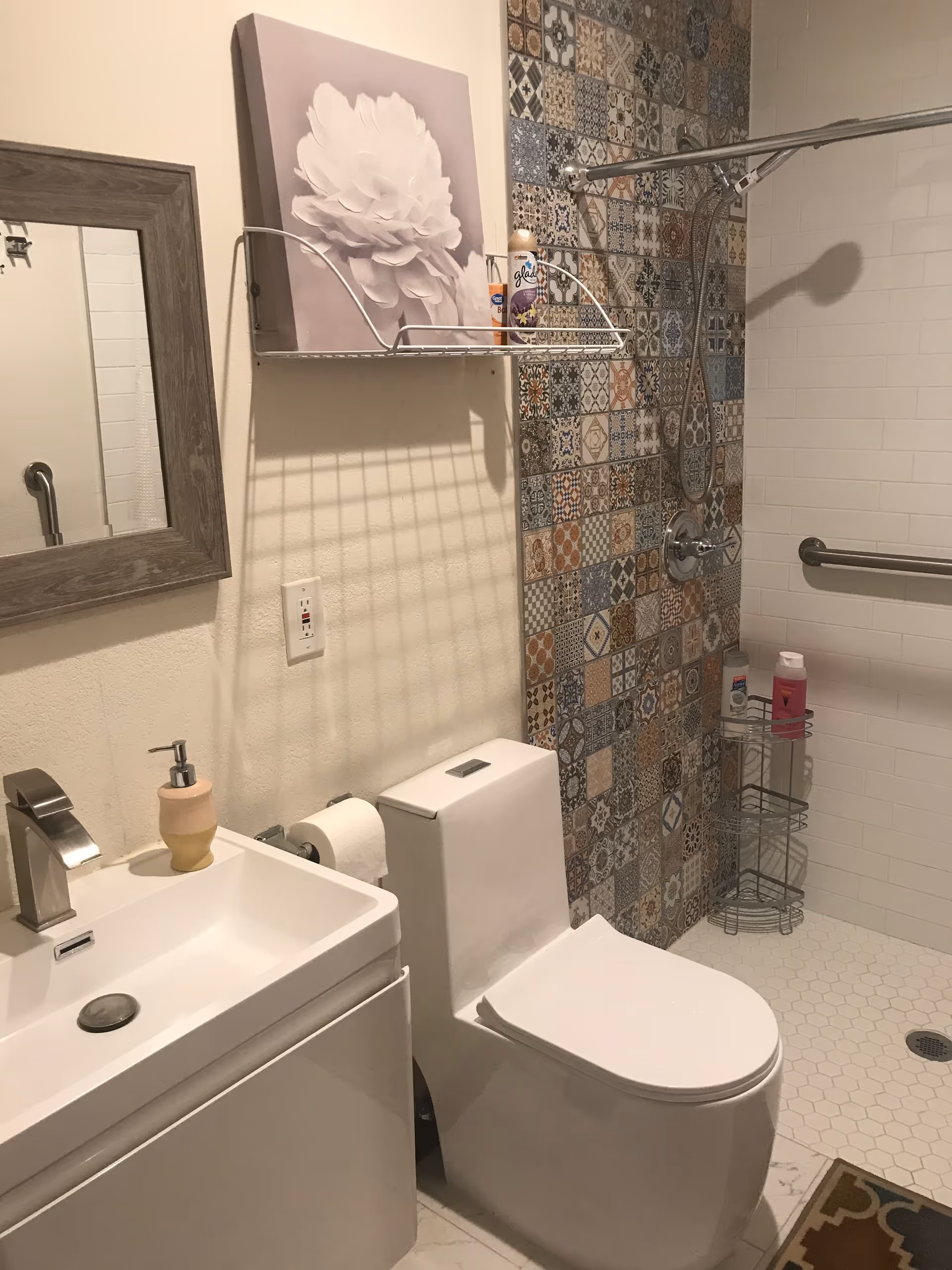 Bathroom in senior living facility with sink, toilet, mirror, and decorative tiled shower area.