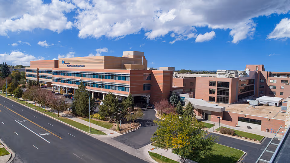 Banner North Colorado Medical Center campus shown from street, brick multi-story hospital under blue sky.