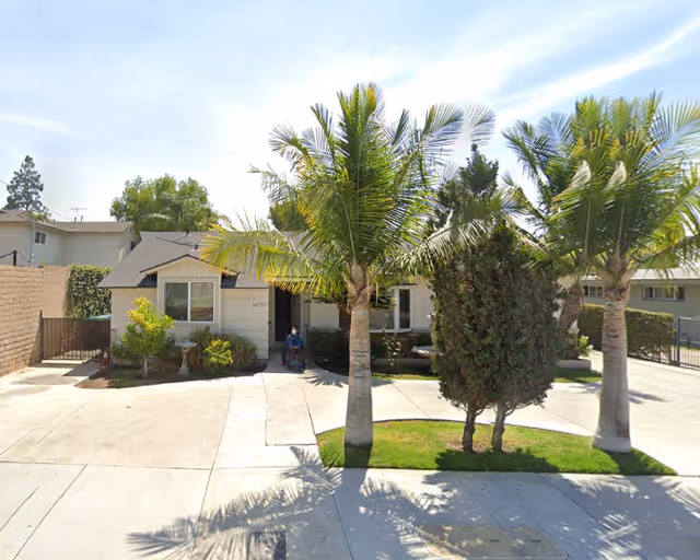 Front exterior of a single-story senior care facility with palm trees and a driveway.