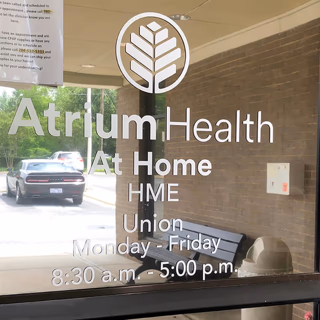 Glass entrance door with Atrium Health At Home HME Union signage and hours.