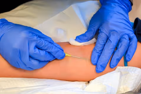 Blue-gloved hands insert needle into resident's arm during procedure.