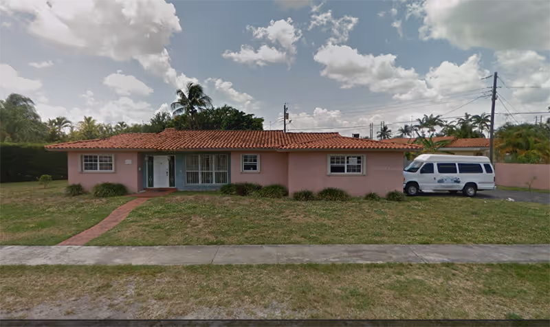 Single-story pink building with red-tiled roof, palm trees, and a white van parked outside.